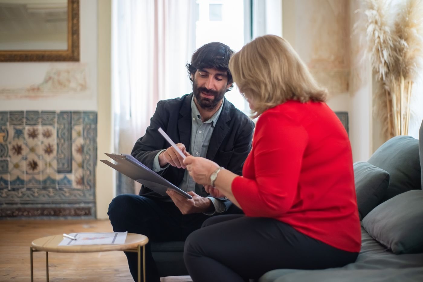 Consultor conversando com uma empresária sobre documentos, sentados num sofá