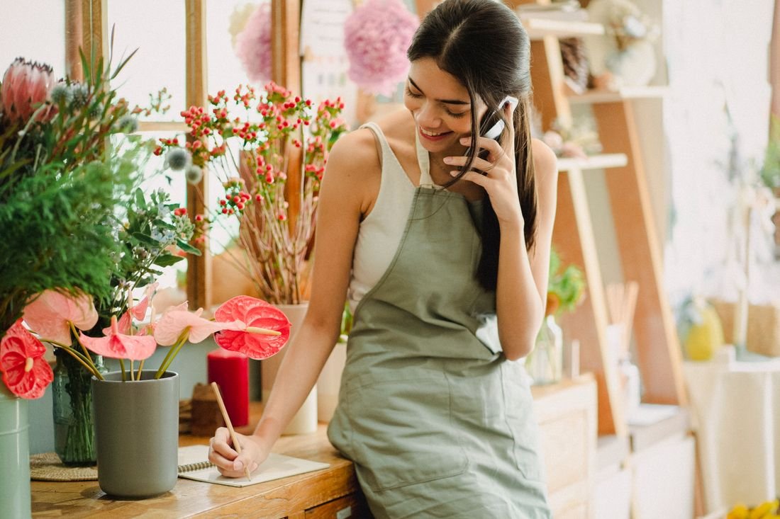 Dona de uma floricultura anotando um pedido enquanto fala ao telefone